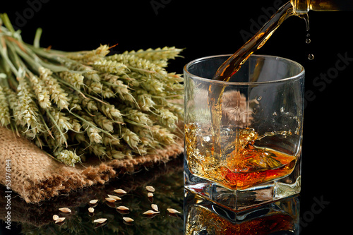 Pouring whiskey into glass, on black background