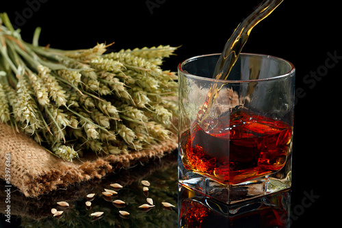 Pouring whiskey into glass, on black background