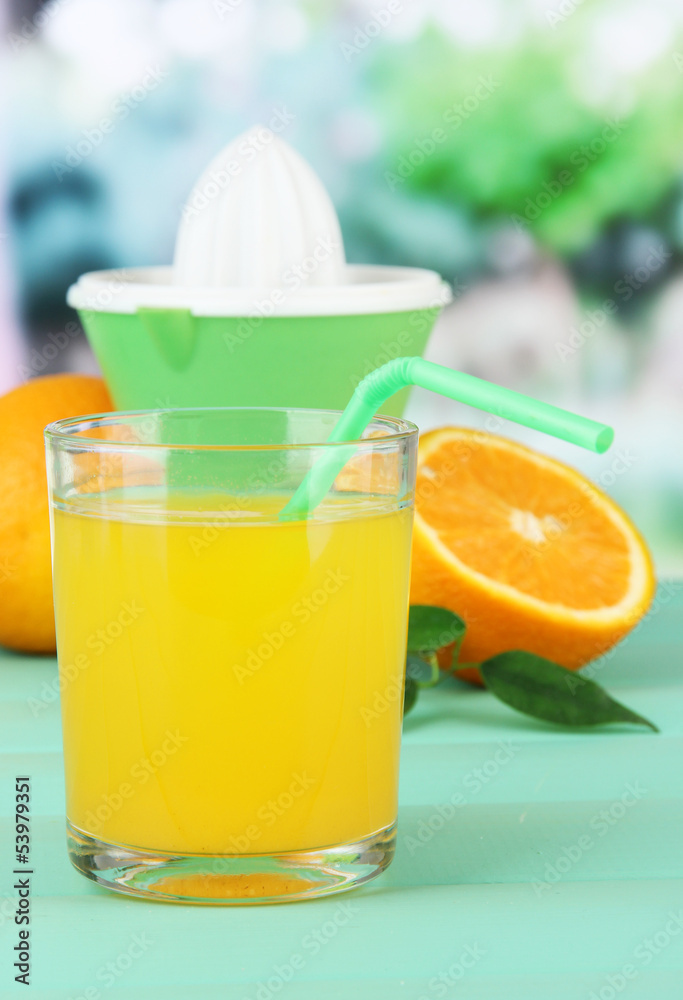 Fototapeta premium Freshly squeezed orange juice in glass with green straw, citrus juicer, and whole oranges on wooden table