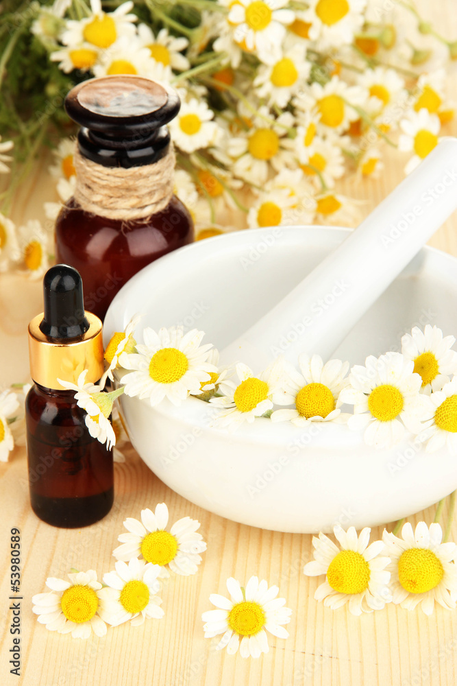 Essential oil and chamomile flowers in mortar on wooden table Essential oil and chamomile flowers in mortar on wooden table