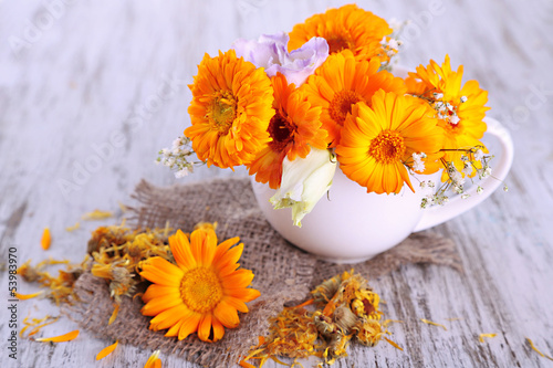 Calendula flowers in cup on wooden background