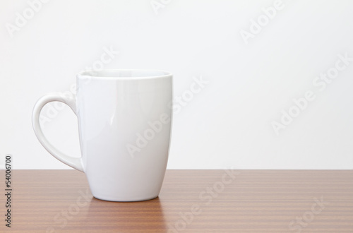 White mug on dark wooden table with white wall