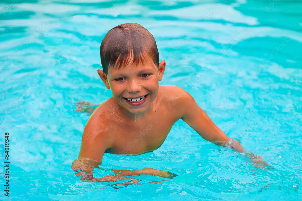 Smiling boy swims in pool on summer vacations