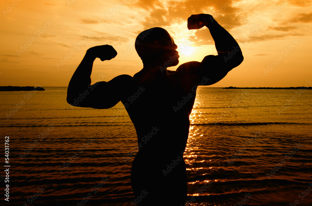 Silhouette of bodybuilder posing at the sunrise on the beach