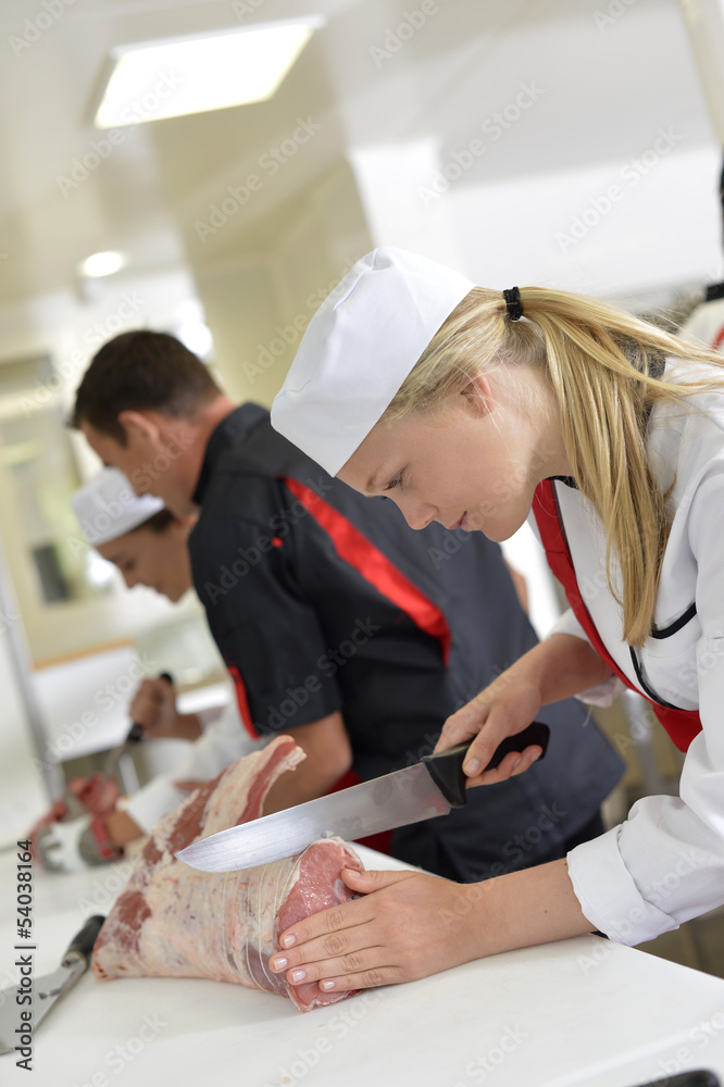 Fototapeta premium Girl cutting meat during butcher training course