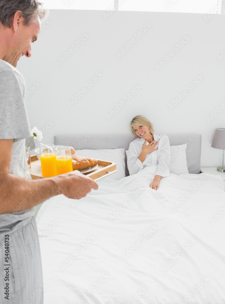 Man bringing breakfast in bed to his surprised partner Man bringing breakfast in bed to his surprised partner