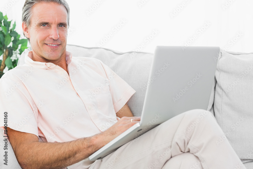Cheerful man on his couch using laptop looking at camera Cheerful man on his couch using laptop looking at camera