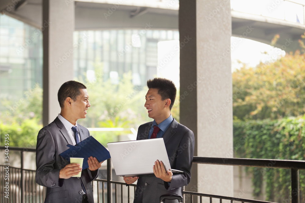 Two young businessmen working outdoor, looking at each other Two young businessmen working outdoor, looking at each other