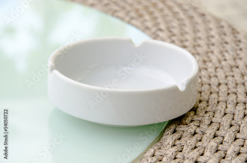 Single white ashtray standing on the glass table of street cafe