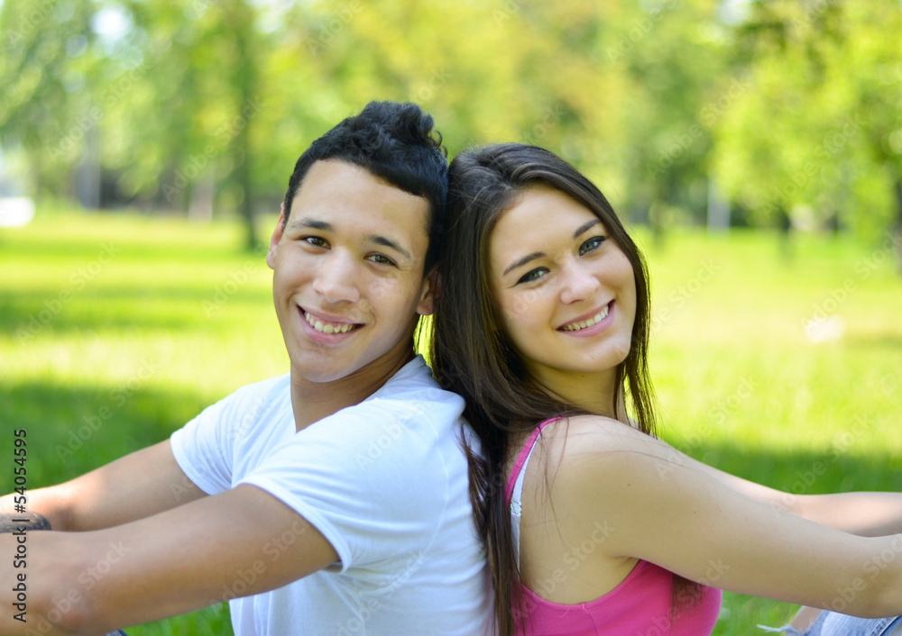Happy young couple back to back in park Happy young couple back to back in park