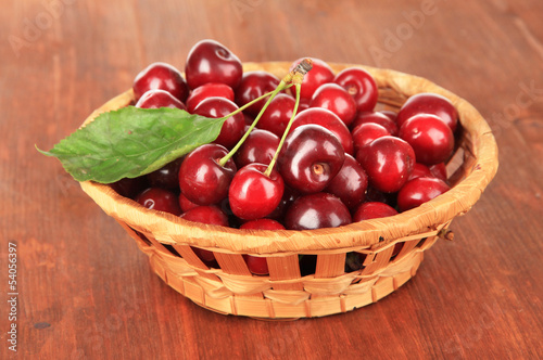 Cherry berries in wicker basket on wooden table close-up