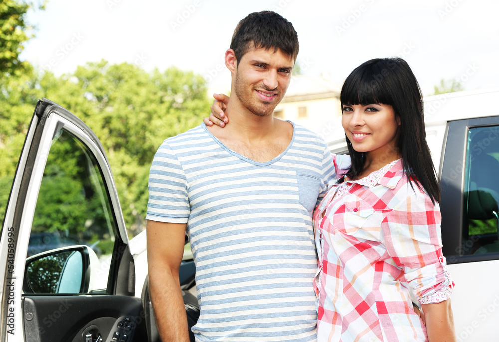 Portrait of happy beautiful couple standing near car