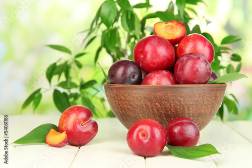 Ripe plums in bowl on wooden table on natural background