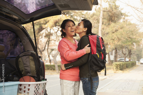 Mother and daughter embracing behind car on college campus © xixinxing