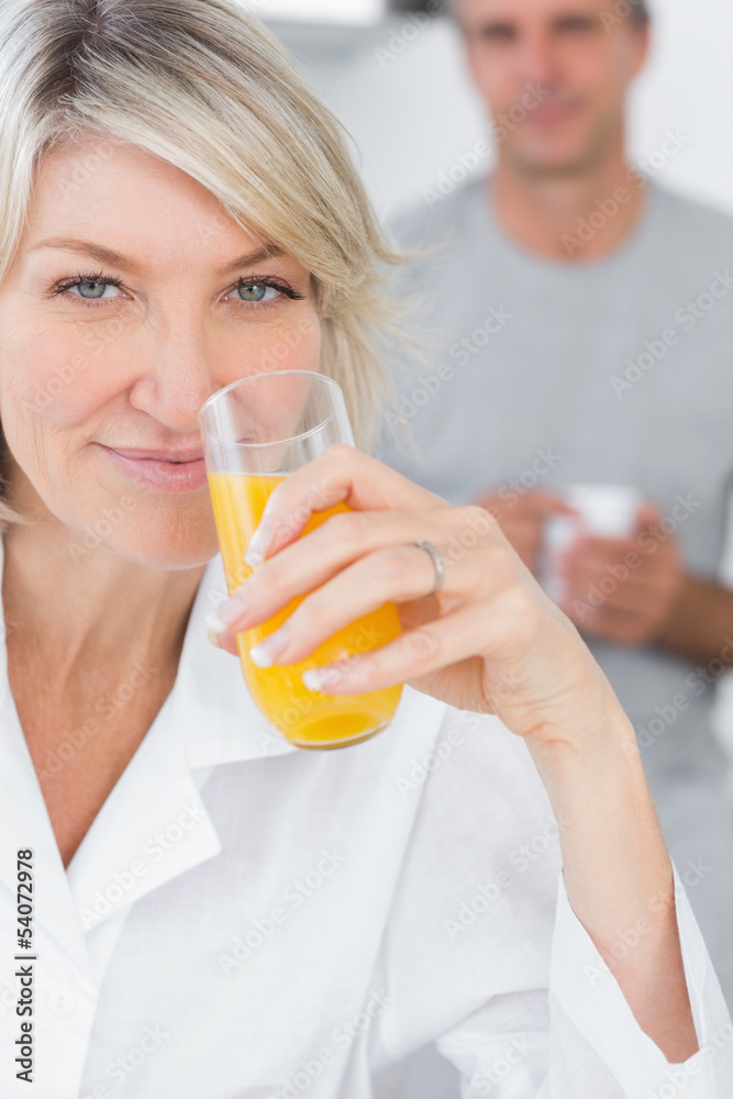 Smiling woman drinking orange juice in kitchen Smiling woman drinking orange juice in kitchen