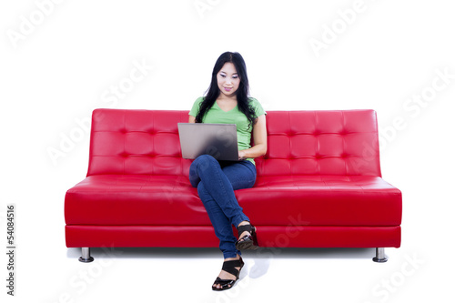 Beautiful female using laptop on red sofa - isolated