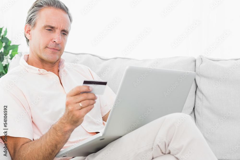 Man on his couch using laptop for online shopping Man on his couch using laptop for online shopping