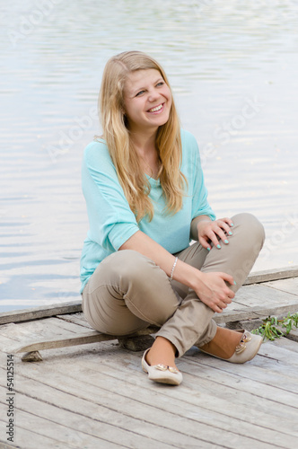 Young woman sitting on pier and smiling © stormy
