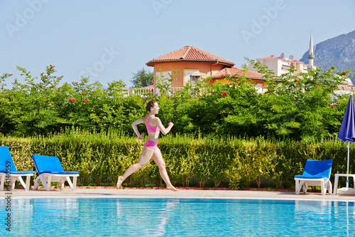 Young woman runs at poolside around pool © Pavel Losevsky