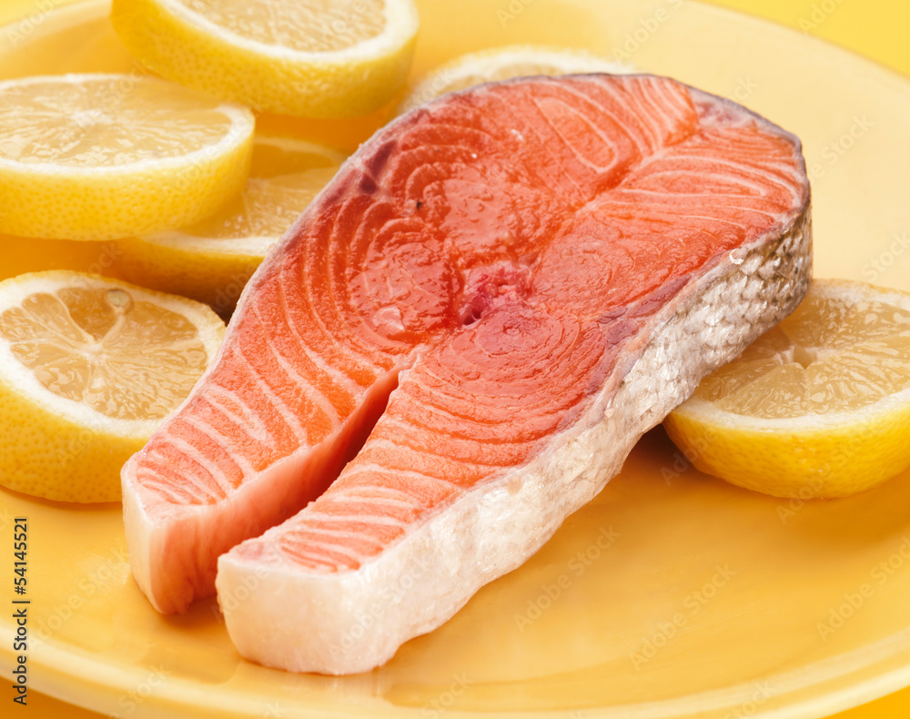 filet of raw salmon on lemons in yellow plate.