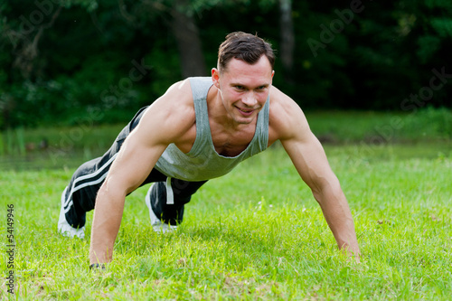 Muscle man doing fitness exercise on the grass in the park
