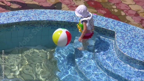 The little girl plays with a ball in water pool