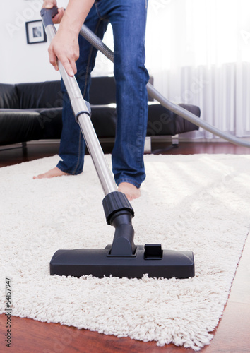 Happy man is cleaning in the modern room with vacuum.