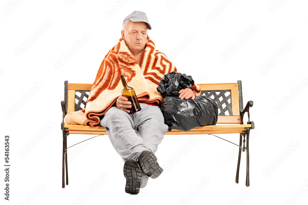 Drunk homeless mature man sitting on a bench and holding a bottl
