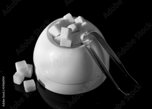 Refined sugar in white sugar bowl on black background photo