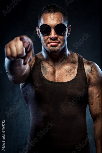 Muscular handsome young man in sunglasses pointing on you