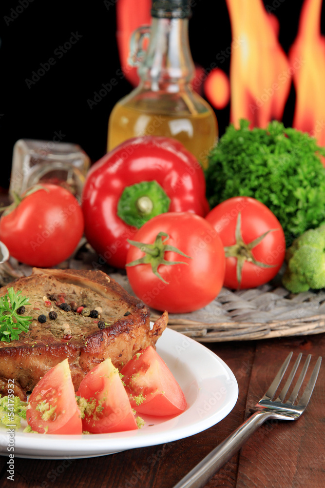 Piece of fried meat on plate on wooden table on fire background