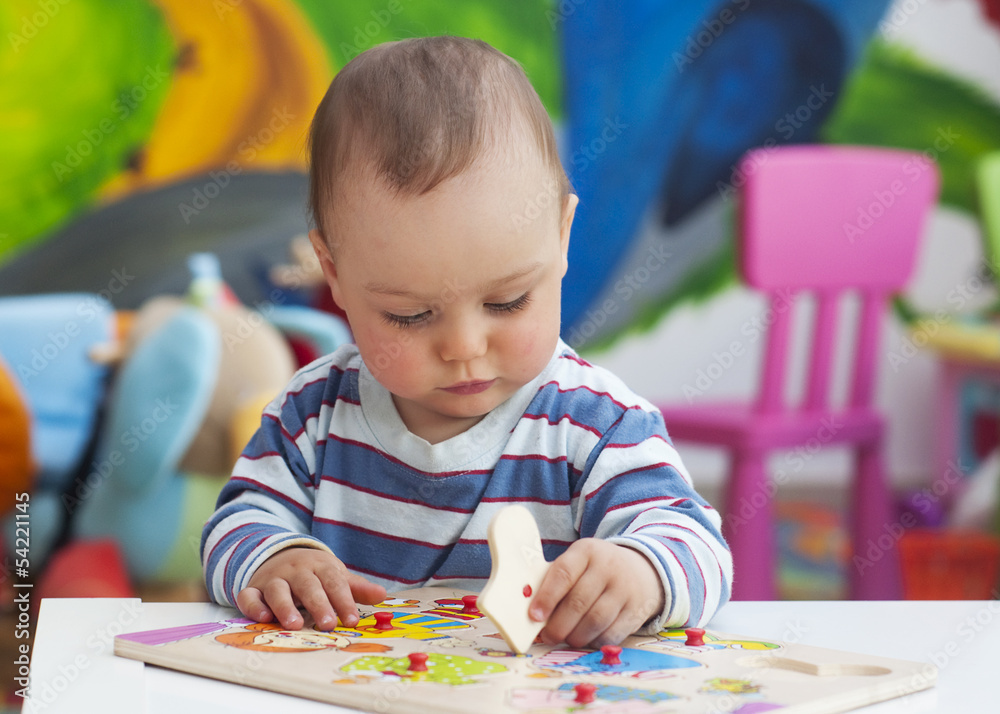 Fototapeta premium Toddler or a baby child playing with puzzle in a nursery.