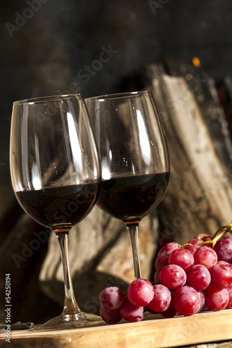 Copas de vino uvas y fuego en chimenea de fondo.
