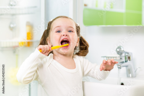 kid girl brushing teeth in bathroom photo
