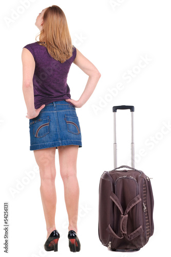 Back view of traveling blonde woman in dress with suitcase looki
