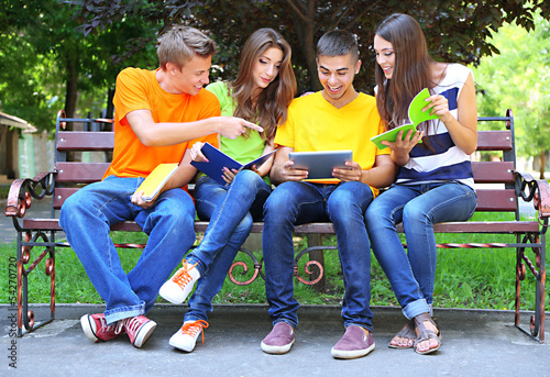 Happy group of young students sitting in park