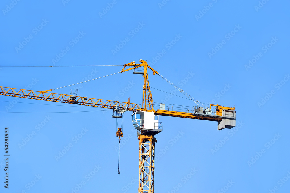 Yellow construction tower crane against blue sky Yellow construction tower crane against blue sky