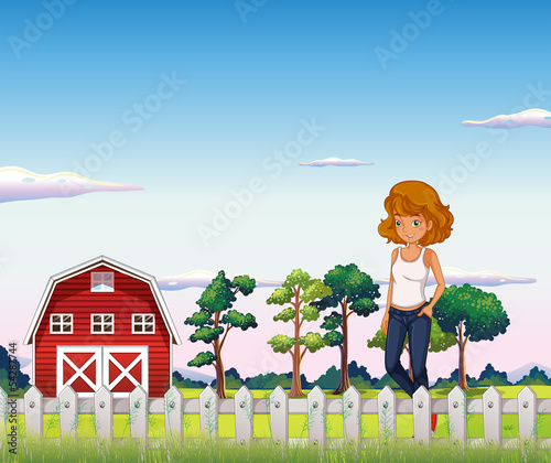 A girl standing near the red barnhouse inside the fence