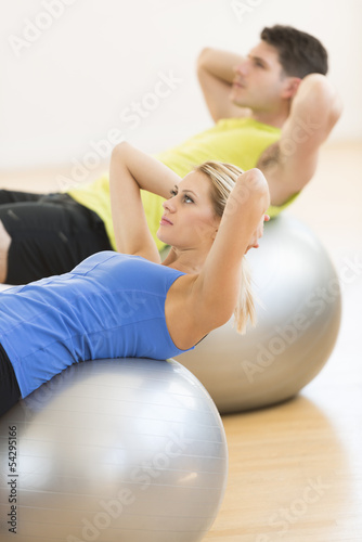 Woman Exercising On Pilate With Man In Background At Club