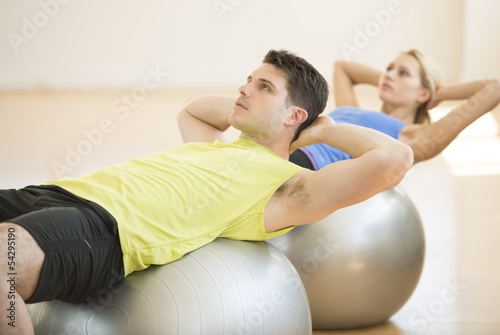 Man Looking Away While Exercising On Fitness Ball At Gym