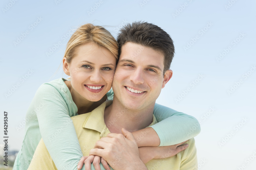 Fototapeta premium Woman Embracing Man From Behind Against Clear Sky