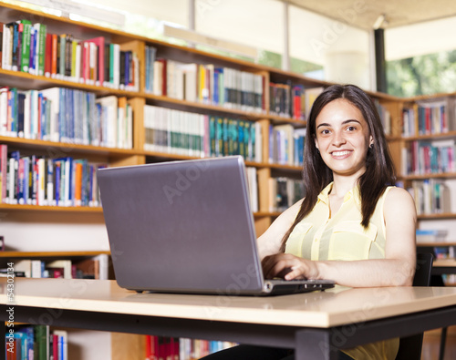 Smiling female student working with laptop in a high school libr
