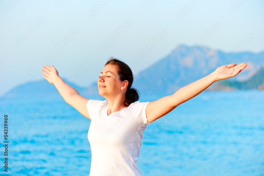 Woman with arms outstretched enjoying the sun by the sea Woman with arms outstretched enjoying the sun by the sea