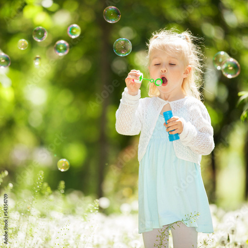 Cute little girl blowing bubbles in the park