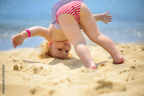 Cute little baby girl making yoga exercises at ocean beach