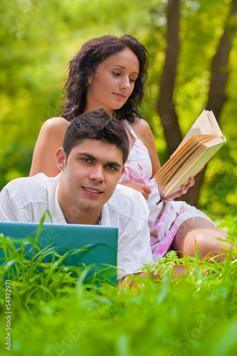 Young couple lying with laptop and book at park