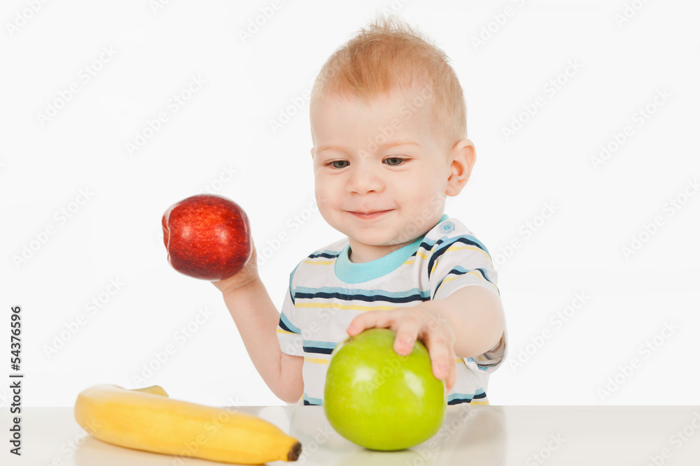 Fototapeta premium Little boy sitting at a table with fruit, on a gray background