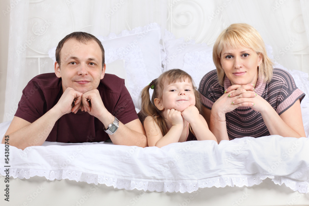 Happy father, little daughter and mother lie on white double bed