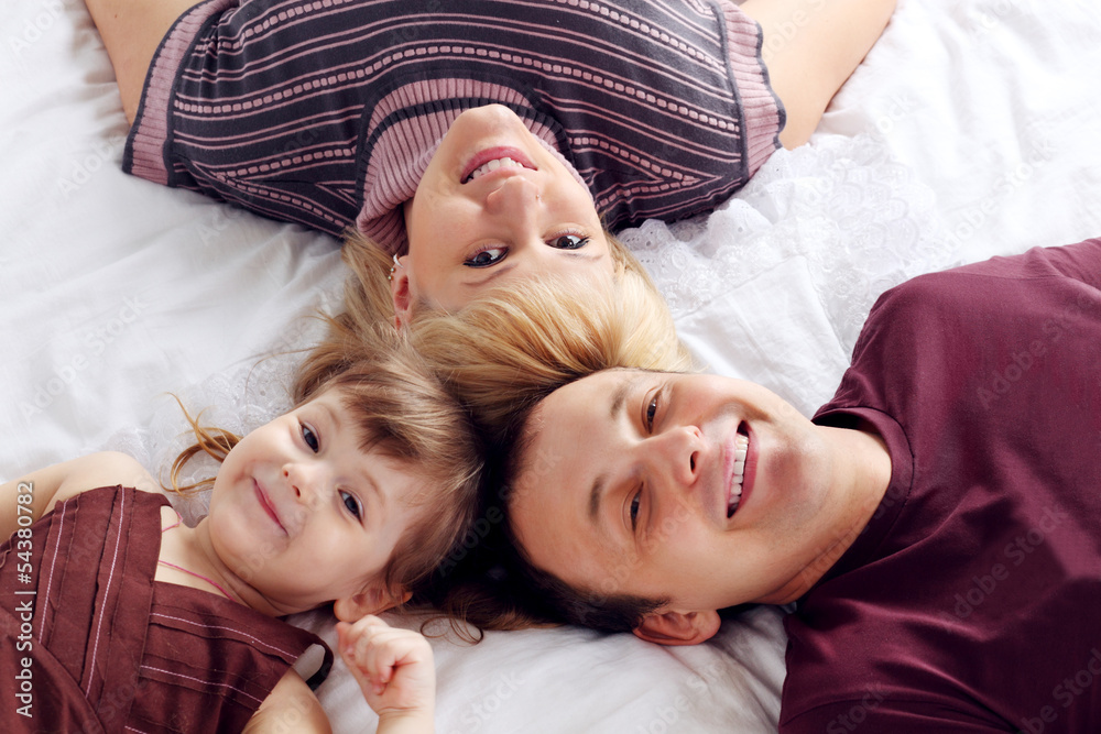 Happy father, little daughter and mother lie on white double bed Happy father, little daughter and mother lie on white double bed