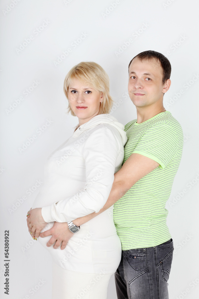 Happy pregnant wife in white and husband hold belly on white bac Happy pregnant wife in white and husband hold belly on white bac